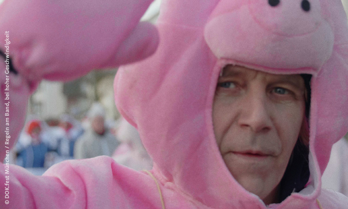 Filmstill aus „Regeln am Band, bei hoher Geschwindigkeit“: Mann im Schweinchen-Kostüm