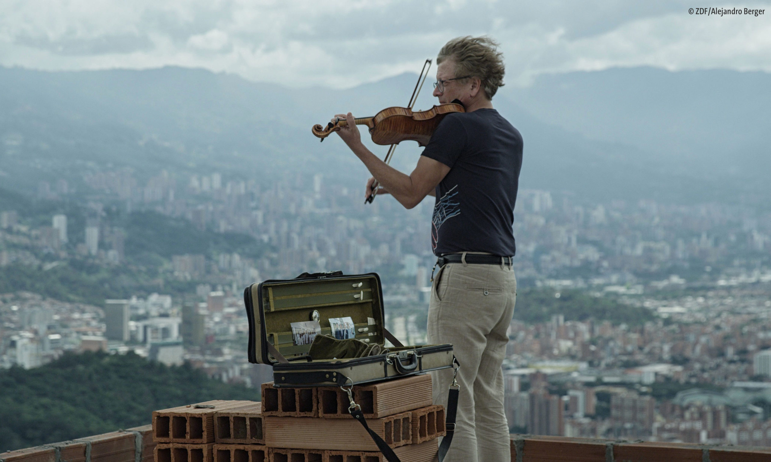 Filmstill aus "Diesen Kuss der ganzen Welt – Beethoven heute": Ein Mann steht auf einem Dach über der kolumbianischen Stadt Medellín und spielt Geige (© ZDF/Alejandro Berger)