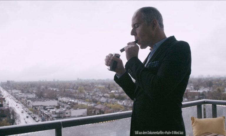 Mann auf einem Balkon zündet sich eine Zigarre