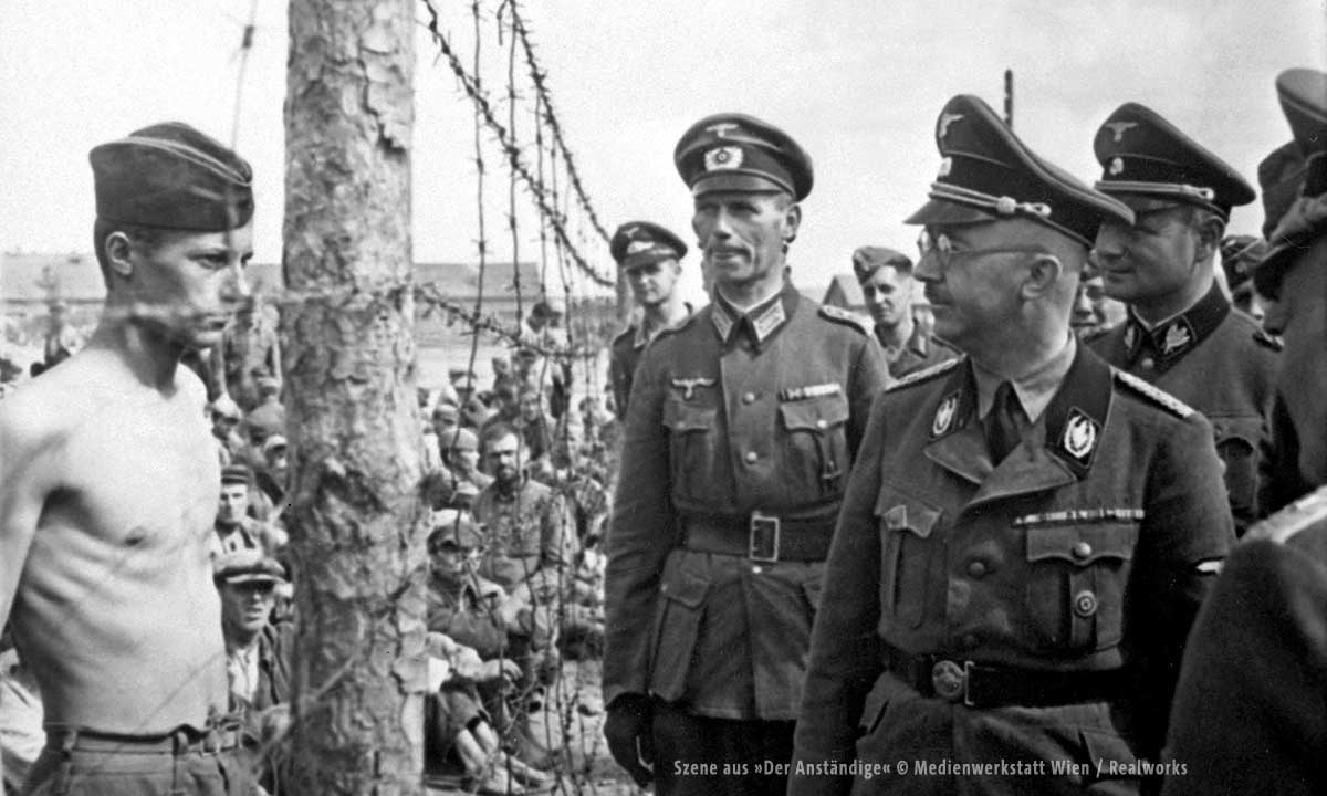 Bild von Heinrich Himmler and einem Zaun stehend gegenüber einem Gefangenen in schwarz/weiß