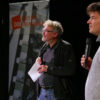 Bild zweier Männer vor einer Leinwand mit Mikrofon