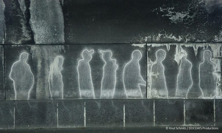 FIlmstill aus "Loveparade - Die Verhandlung": Kunstwerk, das an die Katastrophe 2010 erinntert. Auf einer Wand sind Silhouetten von Menschen aufgemalt. (© Knut Schmitz /DOCDAYS Productions)