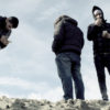 Gruppe von drei Männern steht auf einem Fels. Filmstill aus 